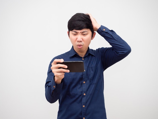 Hombre asiático jugando en el teléfono móvil sintiéndose aburrido tocar su cabeza fondo blanco