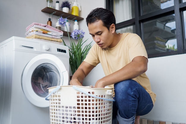 Hombre asiático lavando ropa en casa cargando ropa en la lavadora