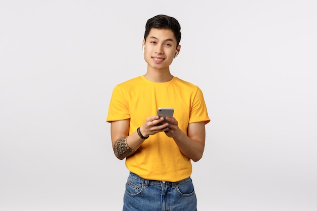 Hombre asiático lindo en camiseta amarilla con smartphone