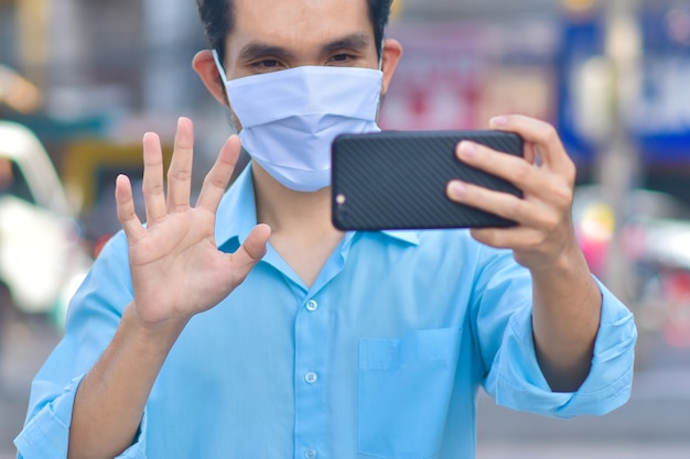 Hombre asiático llamar al teléfono en máscara médica en la calle en la ciudad