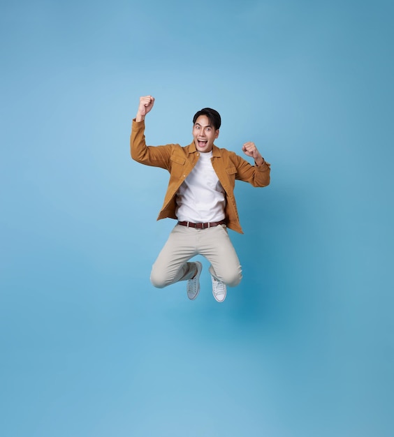 Hombre asiático de longitud completa saltando en el aire con un gesto de sonrisa feliz aislado en fondo azul Hombre feliz saltando alegremente en el espacio de copia Studio corto