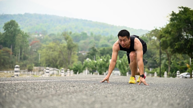 Un hombre asiático maduro, decidido y en forma, está en el camino con una posición inicial