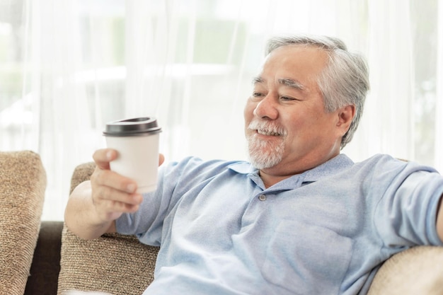El hombre asiático mayor se siente feliz bebiendo café caliente, café con leche caliente, capuchino caliente, disfrute de una taza de café en el sofá en el estilo de vida de la sala de estar, concepto de felicidad senior