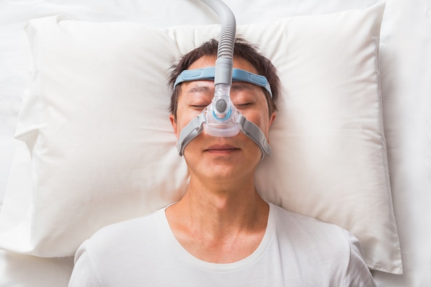 Foto hombre asiático de mediana edad durmiendo en su cama con máscara de cpap para personas con apnea del sueño