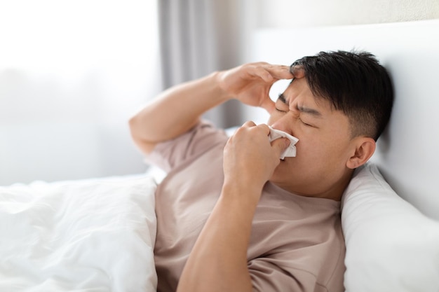 Un hombre asiático de mediana edad enfermo tendido en la cama con gripe.