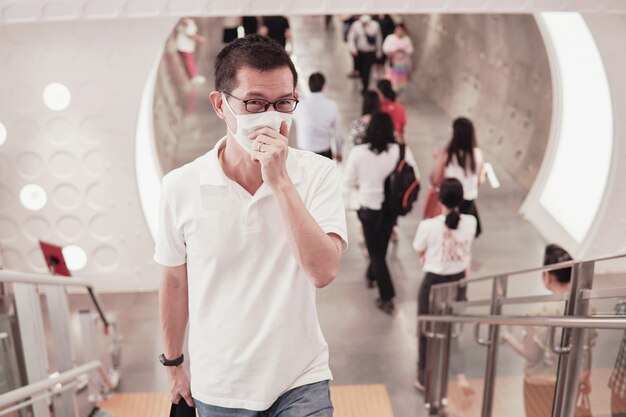 Hombre asiático de mediana edad con gafas y mascarilla médica, tos y estornudos, brote de coronavirus de Wuhan, contaminación del aire y concepto de salud