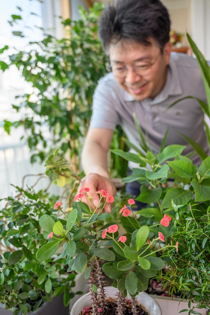 Un hombre asiático de mediana edad que sonríe mientras cuida una cama de flores en su casa.