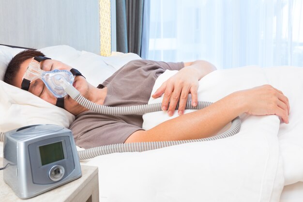 Hombre Asiático Con La Apnea Del Sueño Usando La Máquina De CPAP, Usando La  Máscara De Arnés Que Conecta Al Tubo De Aire, Enfoque Selectivo En El  Hombre Máscara Y El Arnés