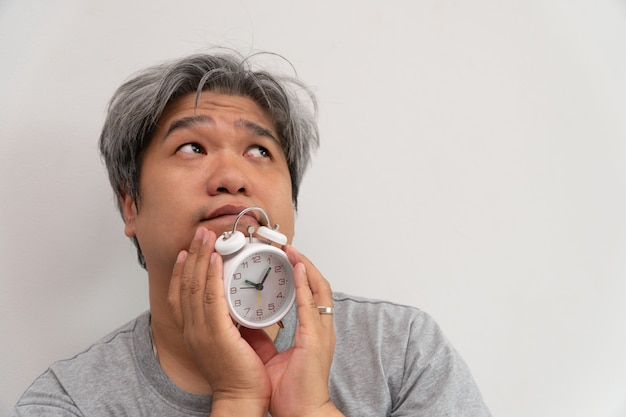 Un hombre asiático de mediana edad sostiene un despertador blanco y su rostro mostraba aburrimiento y se sentía mal.