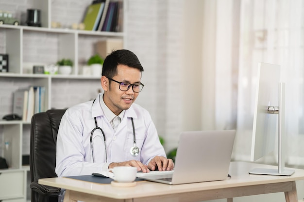 Hombre asiático médico que trabaja con la computadora portátil. Trabajo médico masculino en el hospital de la oficina en casa. Concepto de hospital de salud