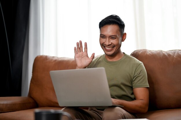 Hombre asiático milenario inteligente que tiene una reunión en línea con su equipo mientras trabaja desde casa