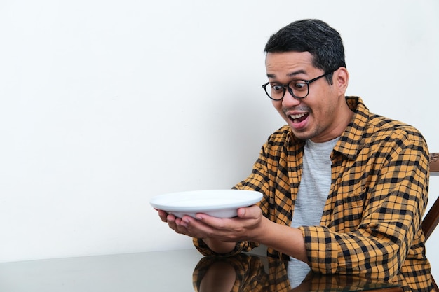 Hombre asiático mirando al plato vacío que sostiene con expresión asombrada