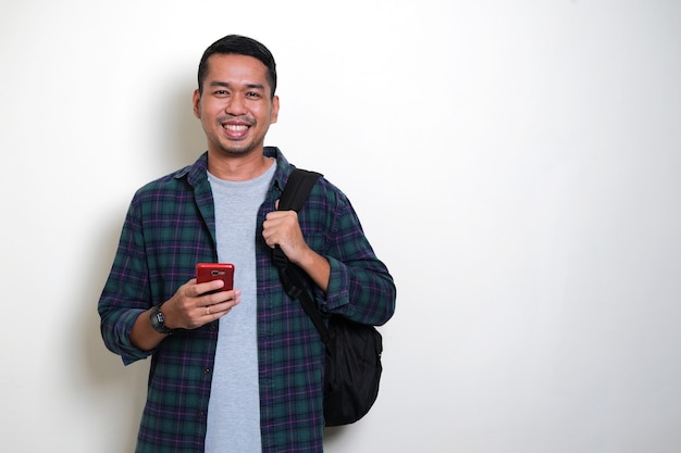 Hombre asiático con mochila shiling feliz mientras sostiene su teléfono móvil