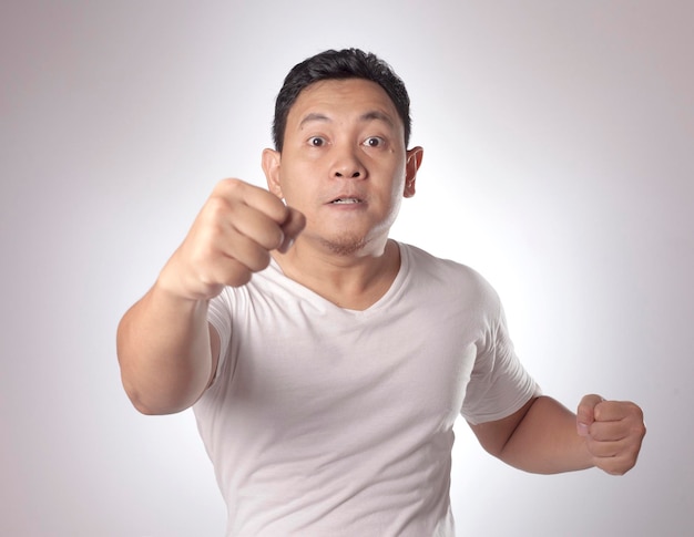 Hombre asiático mostrando una expresión facial cínica infeliz y enojada levantando su puño para desafiar a pelear