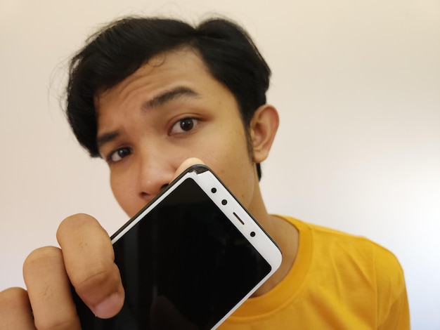 Hombre asiático mostrando smartphone roto con pantalla bloqueada aislado sobre fondo blanco.
