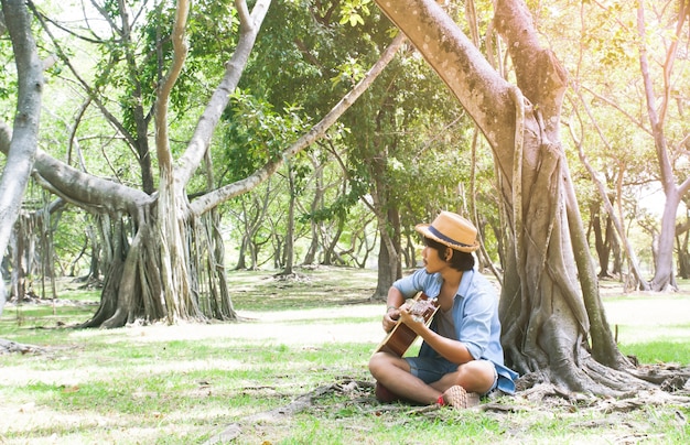 Hombre asiático en pantalones vaqueros ocasionales que tocan la guitarra en el parque