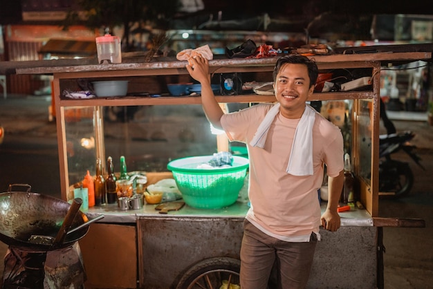 Hombre asiático parado frente al carrito de comida tradicional