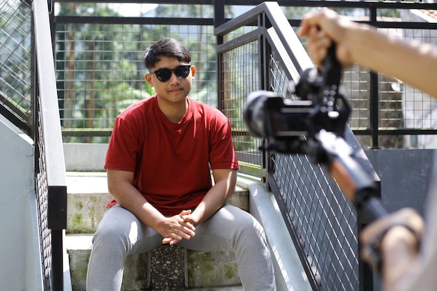 Hombre asiático posando para filmar vlogging al aire libre. Videógrafo sosteniendo cardán con cámara.