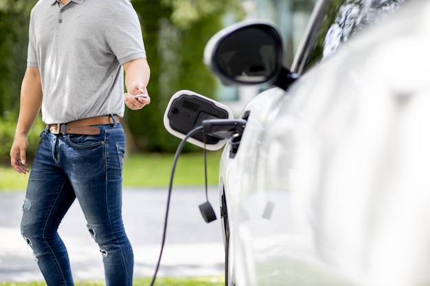 Hombre asiático progresista recarga su auto EV en la estación de carga doméstica