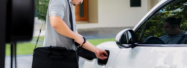 Hombre asiático progresista recarga su auto EV en la estación de carga doméstica