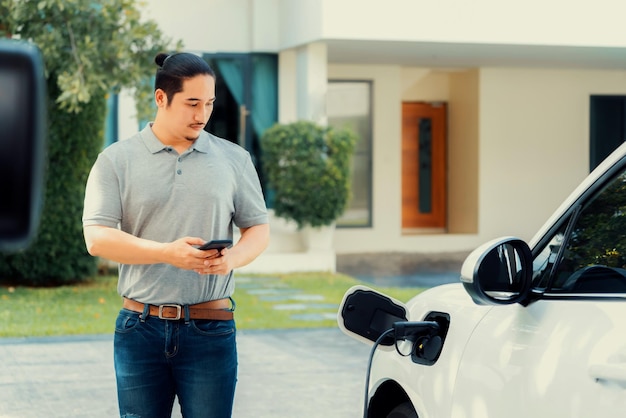 Hombre asiático progresista recarga su auto EV en la estación de carga doméstica