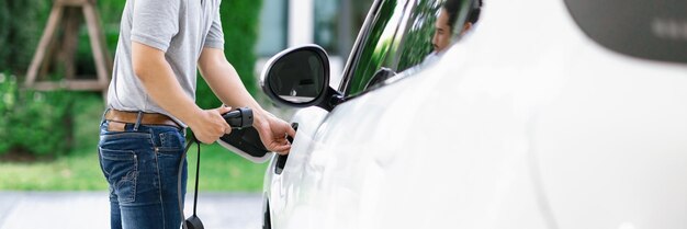 Hombre asiático progresista recarga su auto EV en la estación de carga doméstica