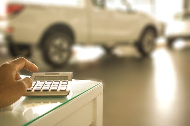 Foto hombre asiático que presiona la calculadora para las finanzas del negocio en la sala de exposición del coche