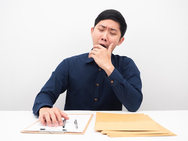 Hombre asiático que se siente somnoliento y bosteza perezoso para trabajar en su lugar de trabajo en la mesa