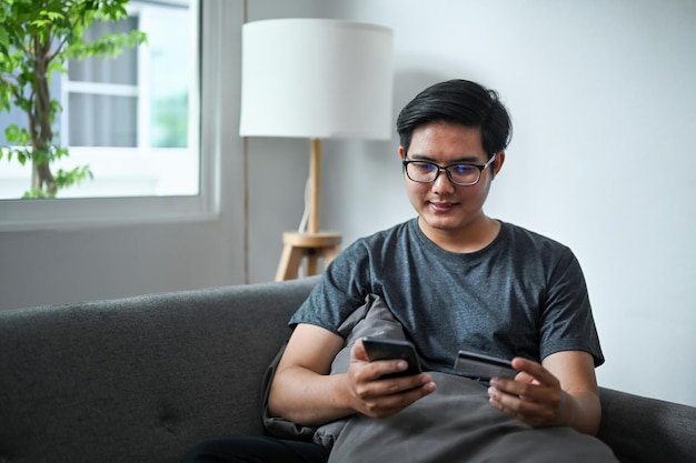 Hombre asiático que usa un teléfono inteligente y tiene una tarjeta de crédito para hornear en línea o comprar en línea