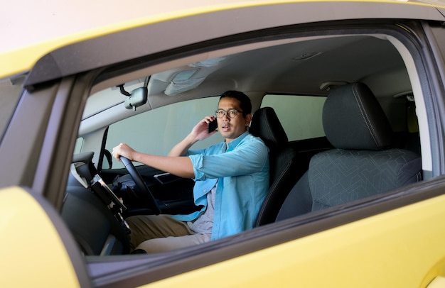 Hombre asiático respondiendo una llamada de teléfono móvil mientras conduce un automóvil