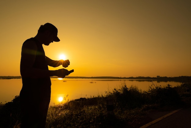 Hombre asiático revisa la hora en su reloj de entrenamiento antes de trotar para un entrenamiento saludable cerca del atardecer