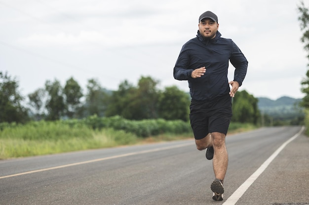 Hombre asiático con ropa deportiva corriendo en la carretera con fondo de montaña. Joven trotando para hacer ejercicio en la naturaleza. estilo de vida saludable y concepto deportivo