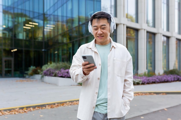 Hombre asiático con ropa informal escuchando música con auriculares programador sonriente y feliz usando