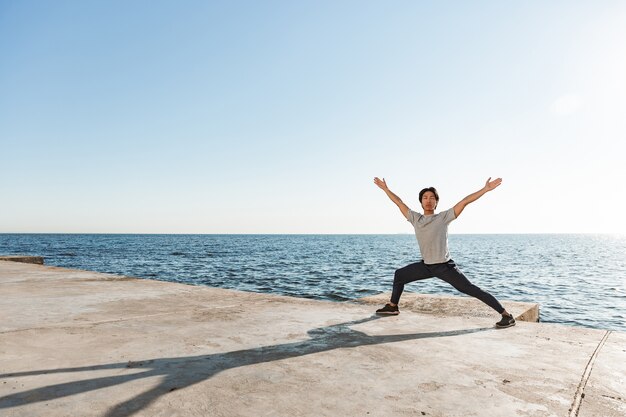 Hombre asiático sano tranquilo haciendo ejercicios de yoga en la playa, equilibrio