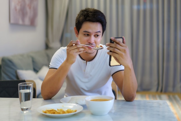 Un hombre asiático sentado en la mesa de la cena y tenía una videollamada hablando con su novia para una cena de distanciamiento social juntos en casa.