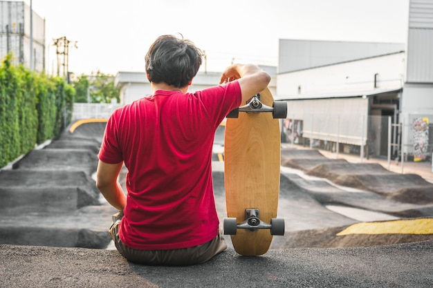 Hombre asiático sentado con surfskate o patineta en Pumptrack Skate Park cuando la hora del amanecer