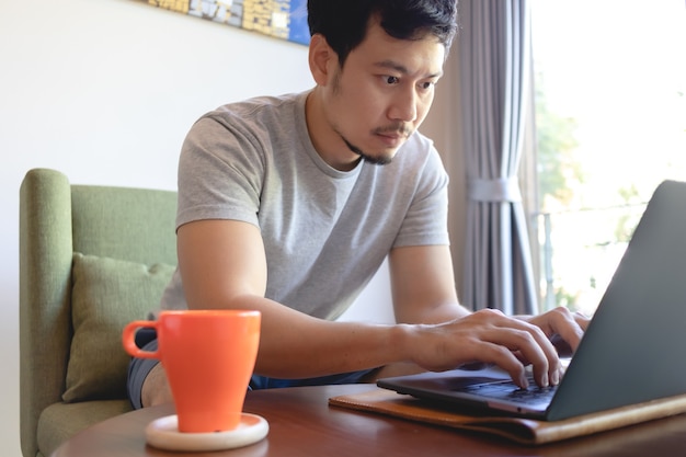 Hombre asiático serio que trabaja en su computadora portátil en la cafetería.