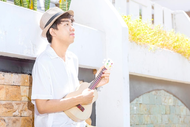 Hombre asiático con sombrero tocando guitarra ukelele