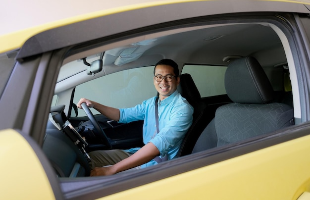 Hombre asiático sonriendo a la cámara desde el interior de su coche