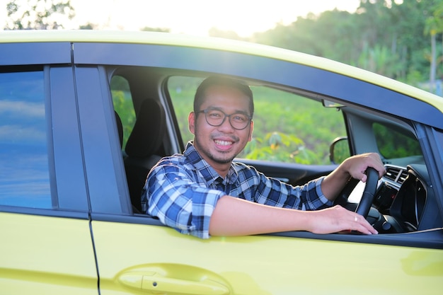 Hombre asiático sonriendo confiado desde dentro de su auto