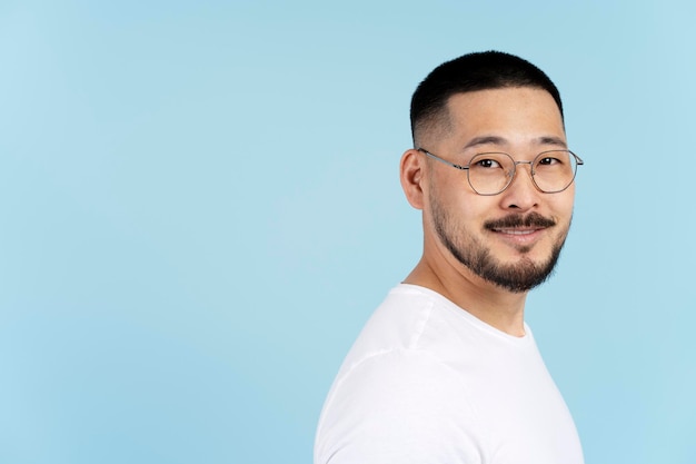 hombre asiático sonriente con anteojos elegantes, camiseta blanca aislada de fondo azul