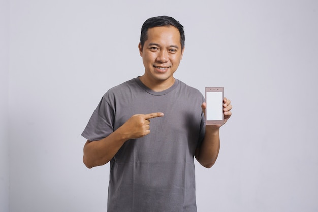 Hombre asiático sonriente apuntando su teléfono inteligente con pantalla en blanco para maqueta