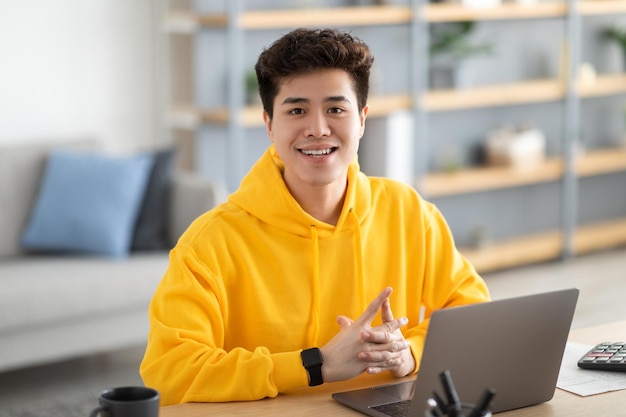 Hombre asiático sonriente confiado posando sentado en el escritorio