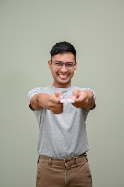 Hombre asiático sonriente entregando una tarjeta de crédito a la cámara mientras está de pie contra un fondo aislado