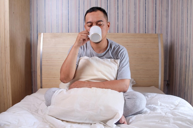 Hombre asiático sonriente feliz bebiendo café en la cama en casa