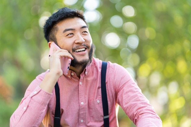 Hombre asiático sonriente hablando con el móvil en un parque