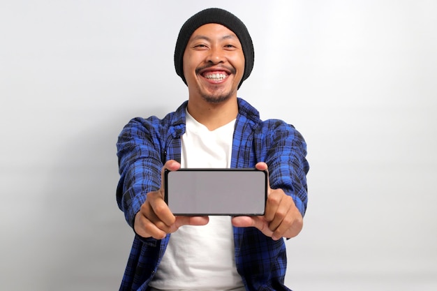 Un hombre asiático sonriente muestra una pantalla blanca en blanco en su teléfono móvil a la cámara