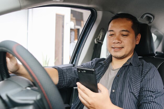 Hombre asiático sonriente o conductor conduciendo un coche y usando un teléfono inteligente