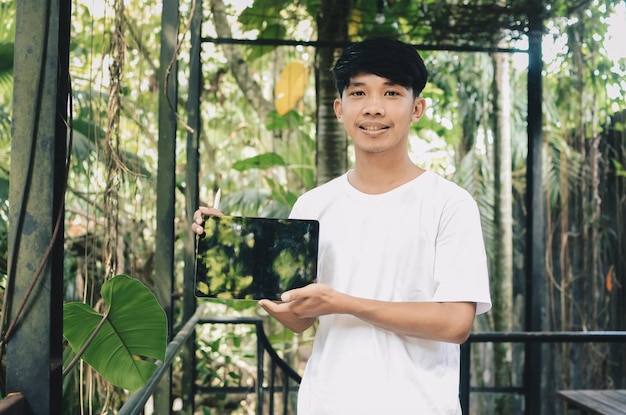 Hombre asiático sonriente que muestra la pantalla de la tableta en el fondo de la naturaleza