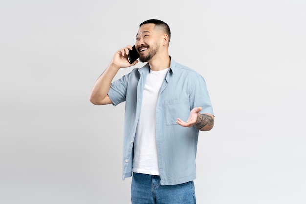 Hombre asiático sonriente con ropa informal elegante hablando por teléfono móvil mirando hacia otro lado